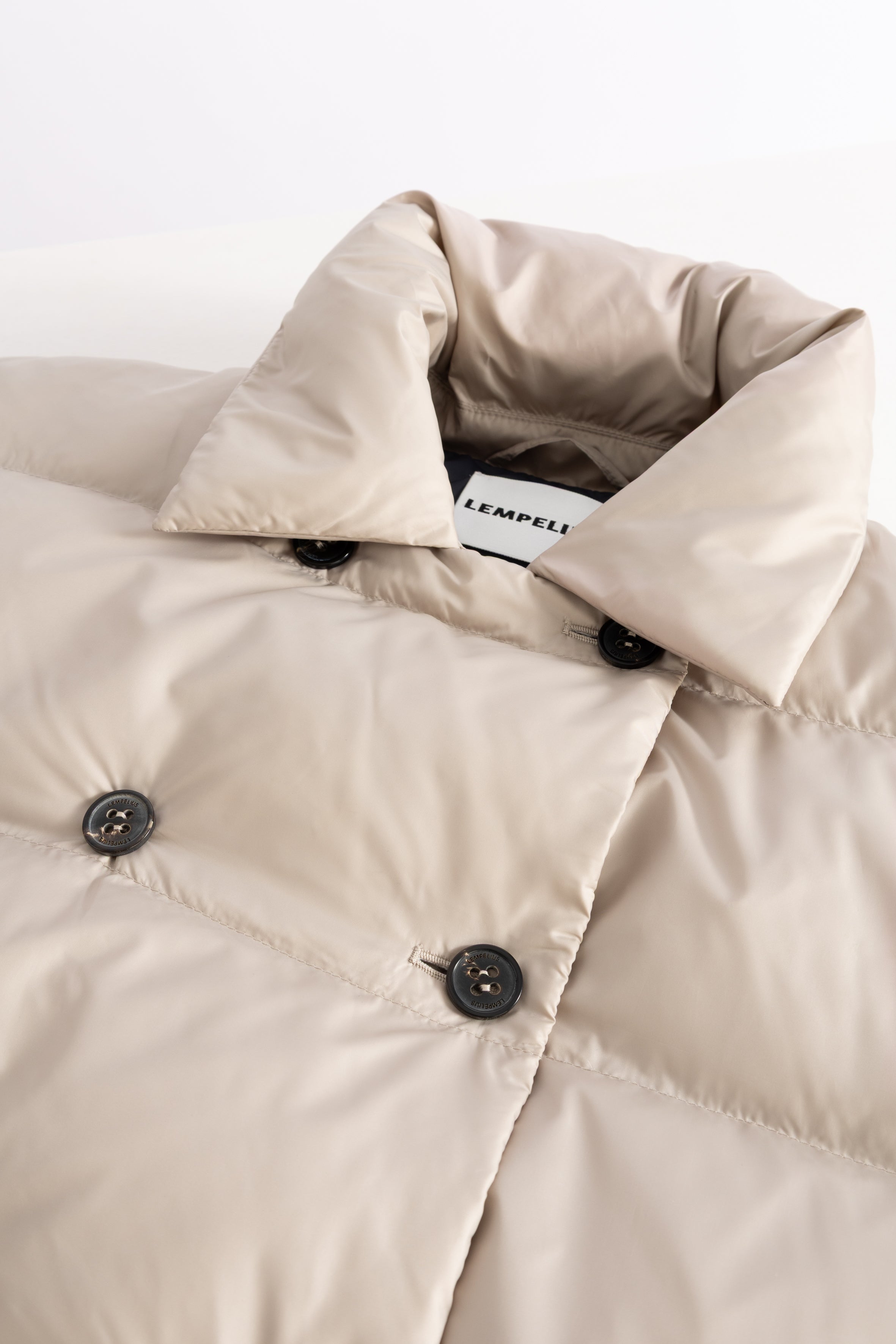 Beige puffer jacket with a visible LEMPELIUS label on a white background with a double breasted horn button closure