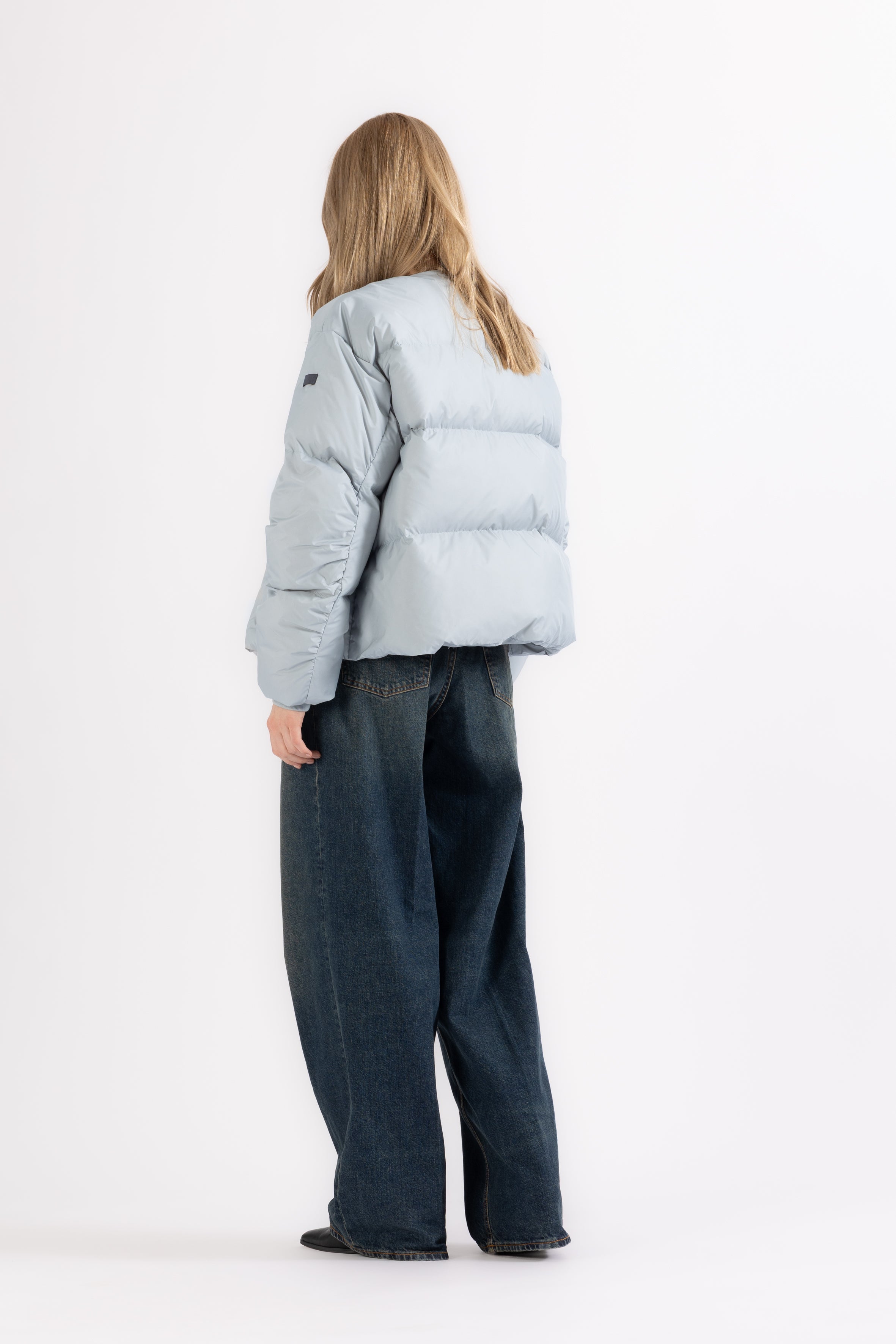 Person wearing a light gray puffer jacket and dark jeans on a white background from the back