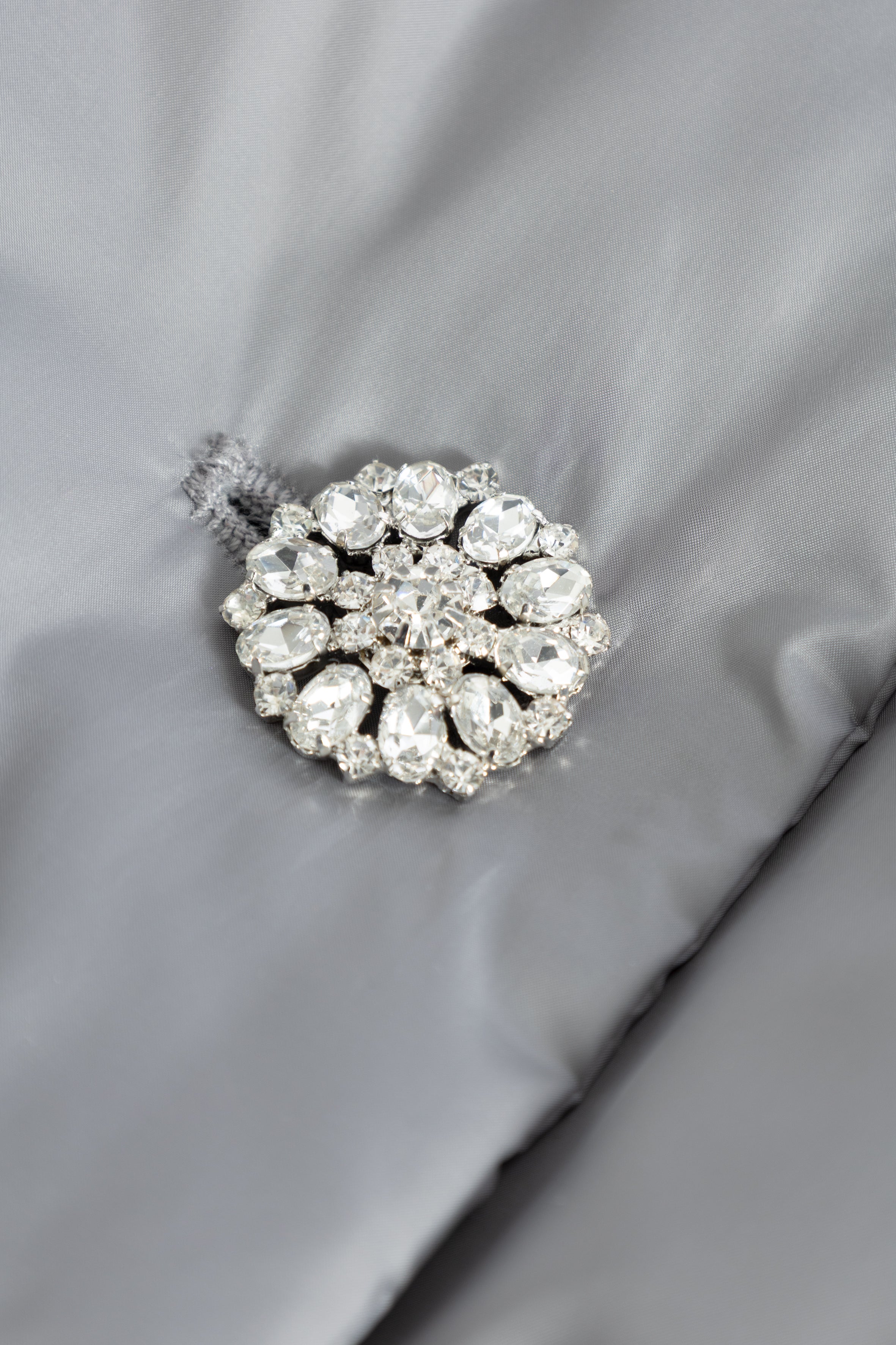 Silver brooch with clear gemstones on a gray fabric background