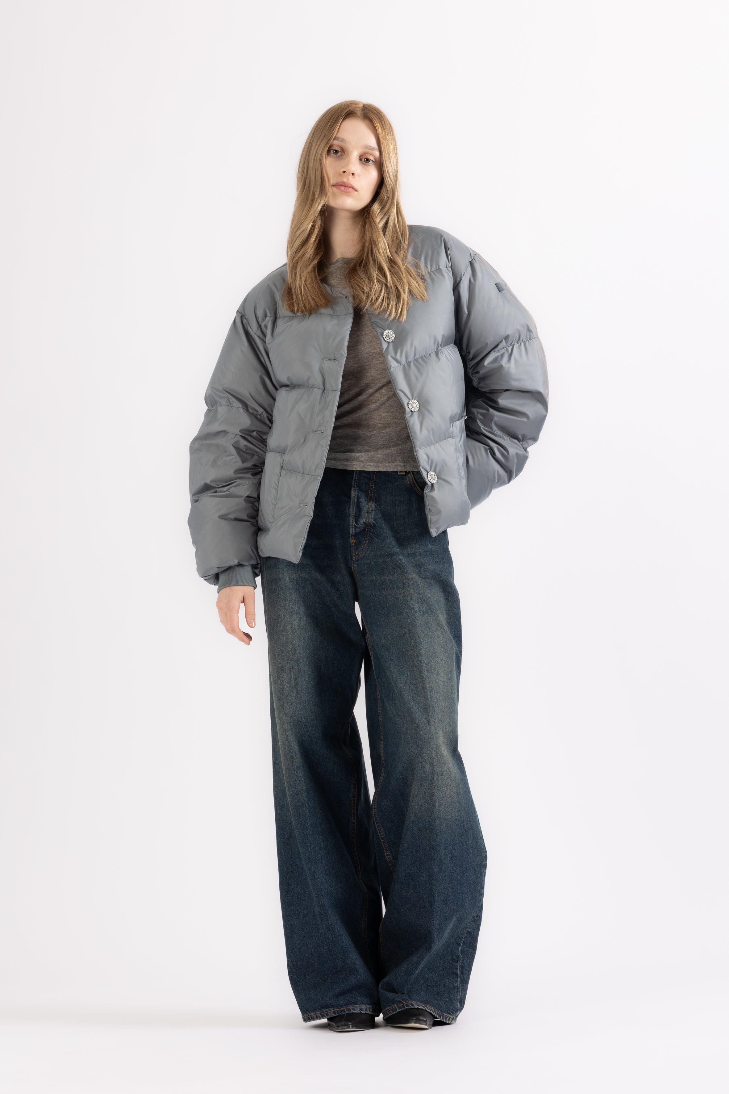 Person wearing a gray puffer jacket and dark jeans on a white background