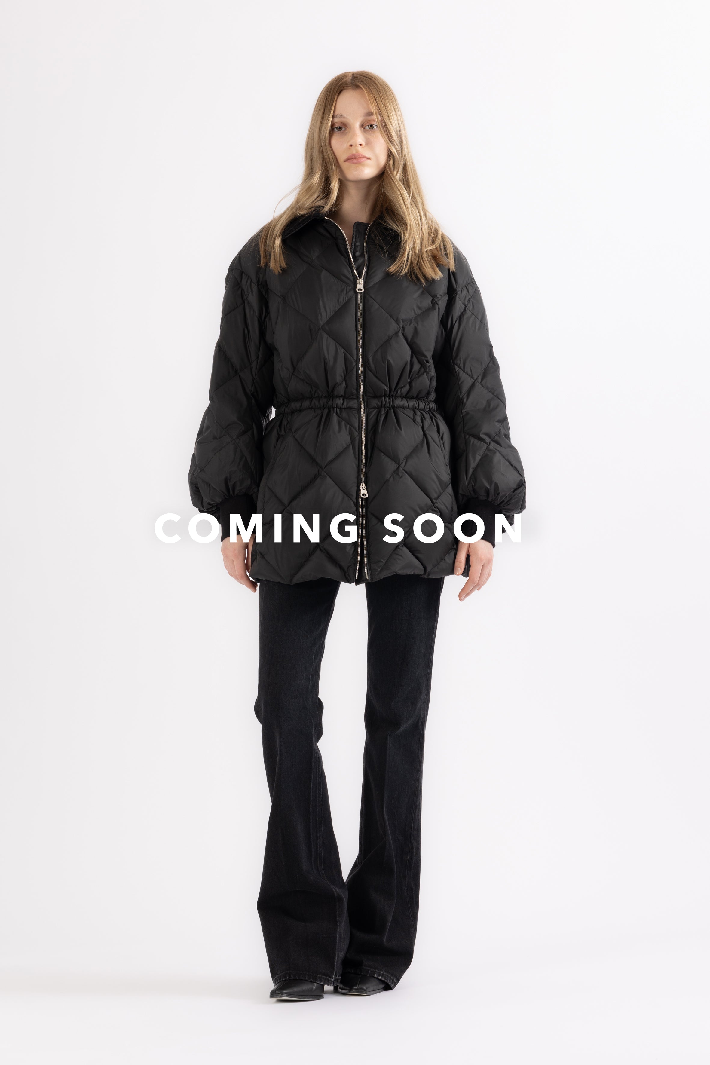 Woman wearing a black quilted puffer jacket with silver zipper on a white background