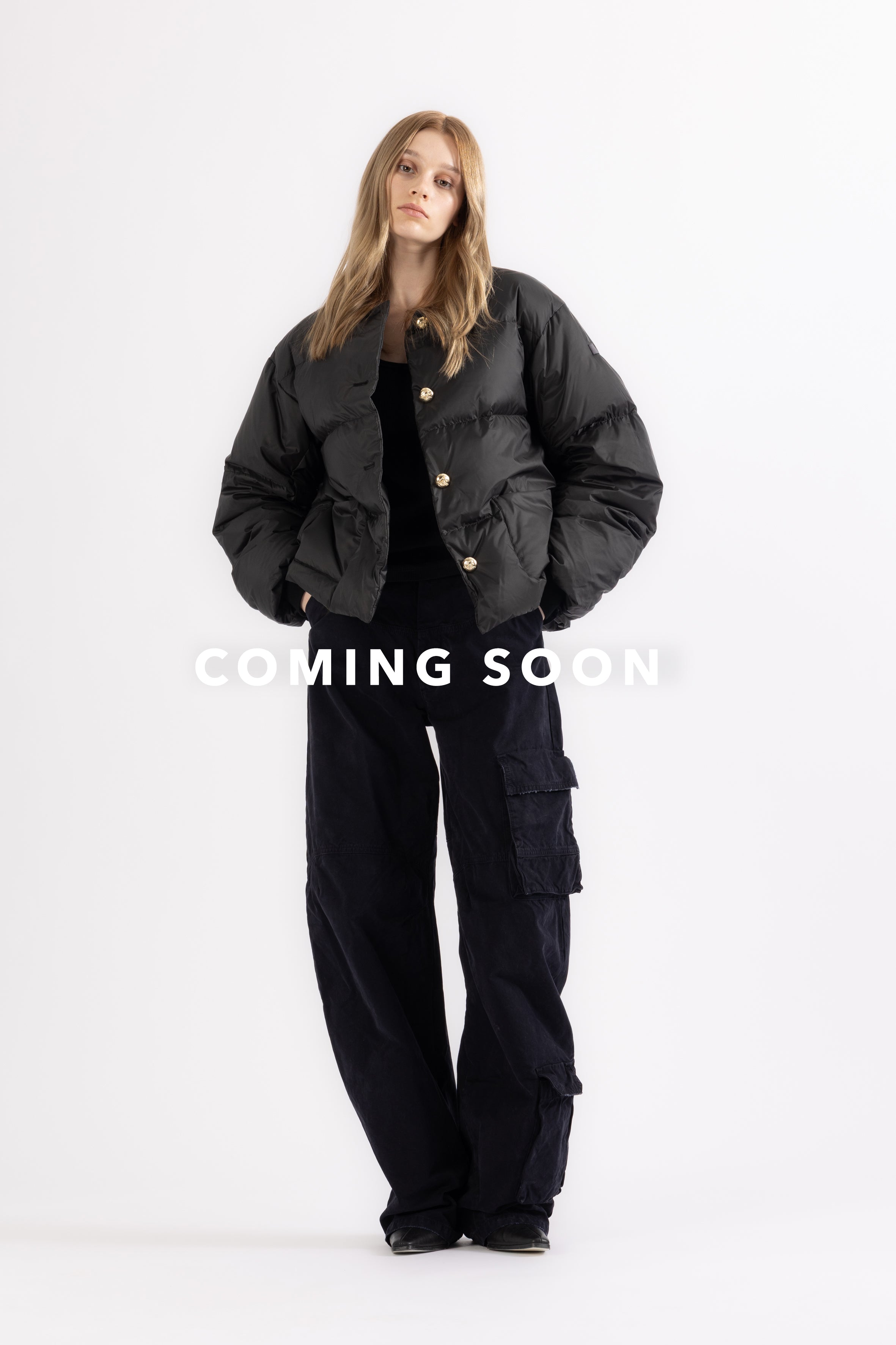 Person wearing a black LEMPELIUS down jacket 278GO with gold buttons and cargo pants on a white background