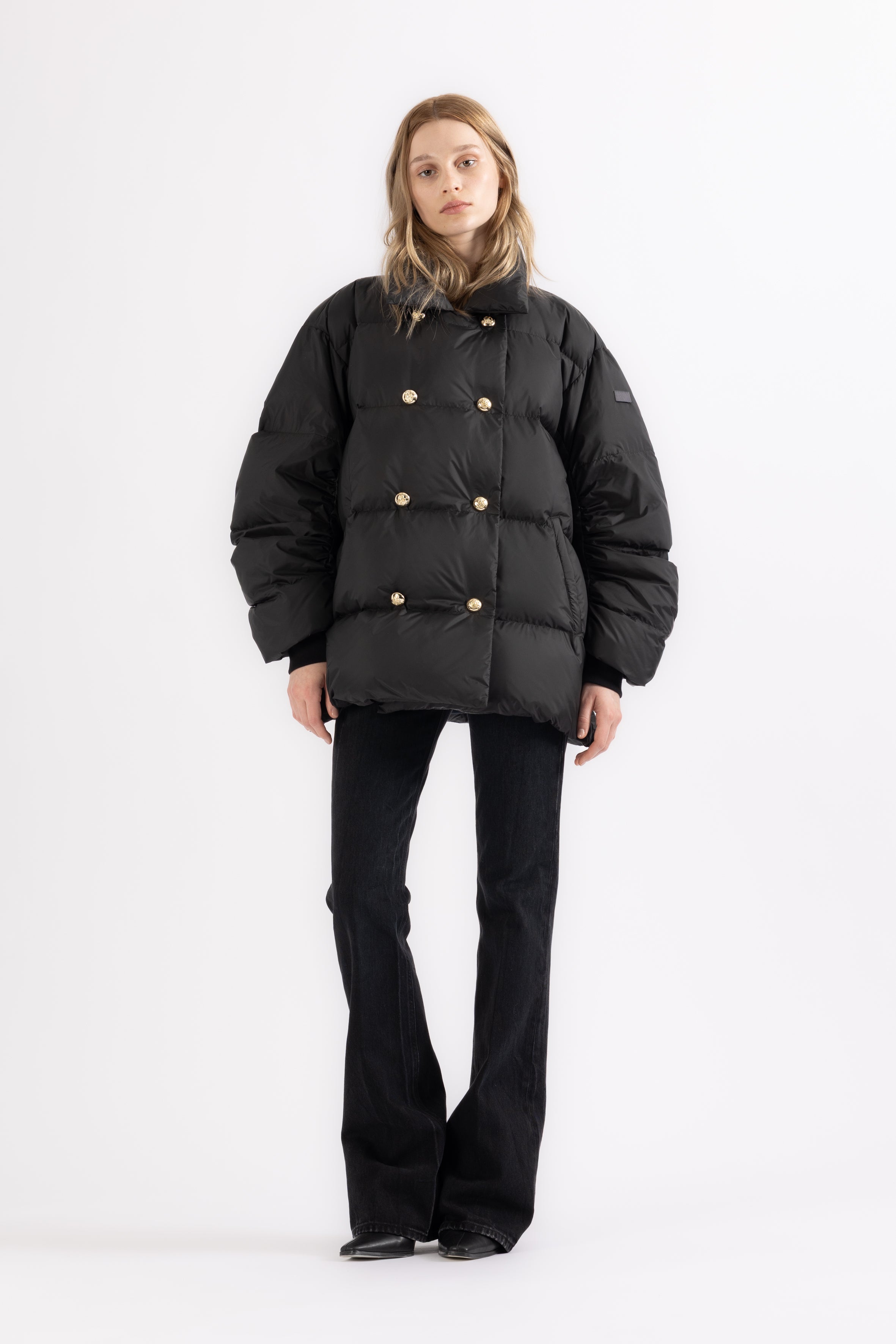 Person wearing a black LEMPELIUS puffer jacket with a double breasted gold button closure on a white background