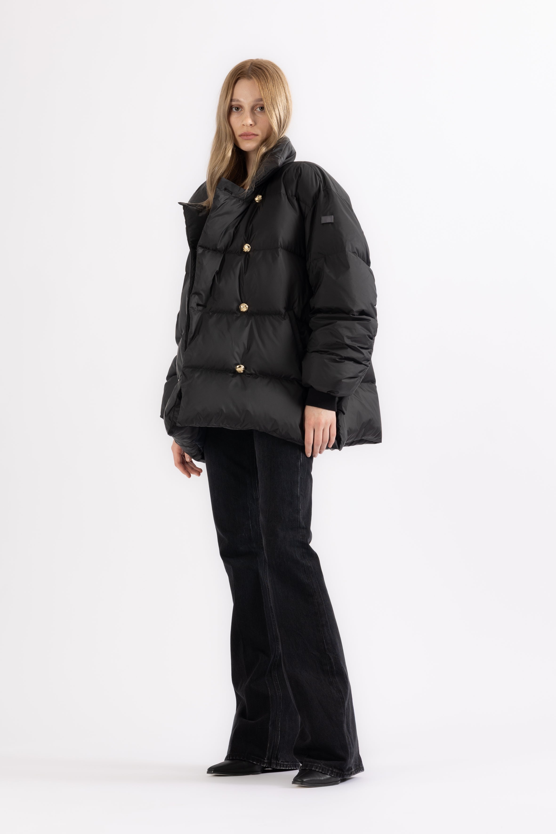 Person wearing a black LEMPELIUS puffer jacket with a double breasted gold button closure on a white background