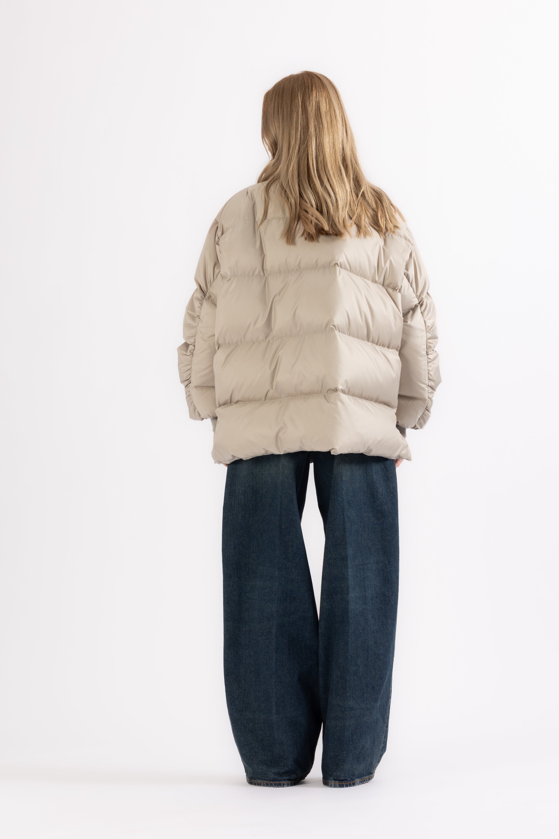 woman wearing a beige, short, double-breasted puffer jacket 270HB ADA with horn button closure on a white background from the back