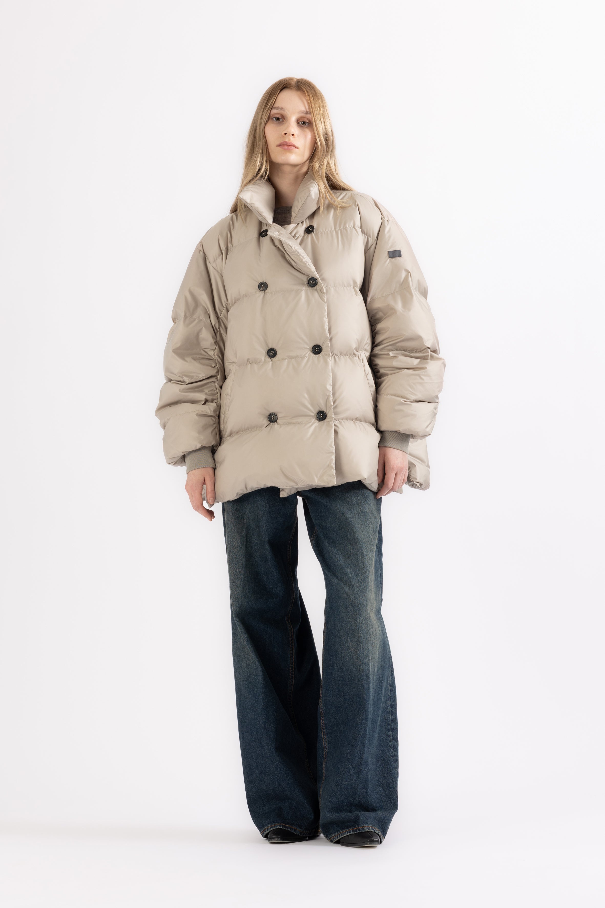 woman wearing a beige, short, double-breasted puffer jacket 270HB ADA with horn button closure on a white background from the front