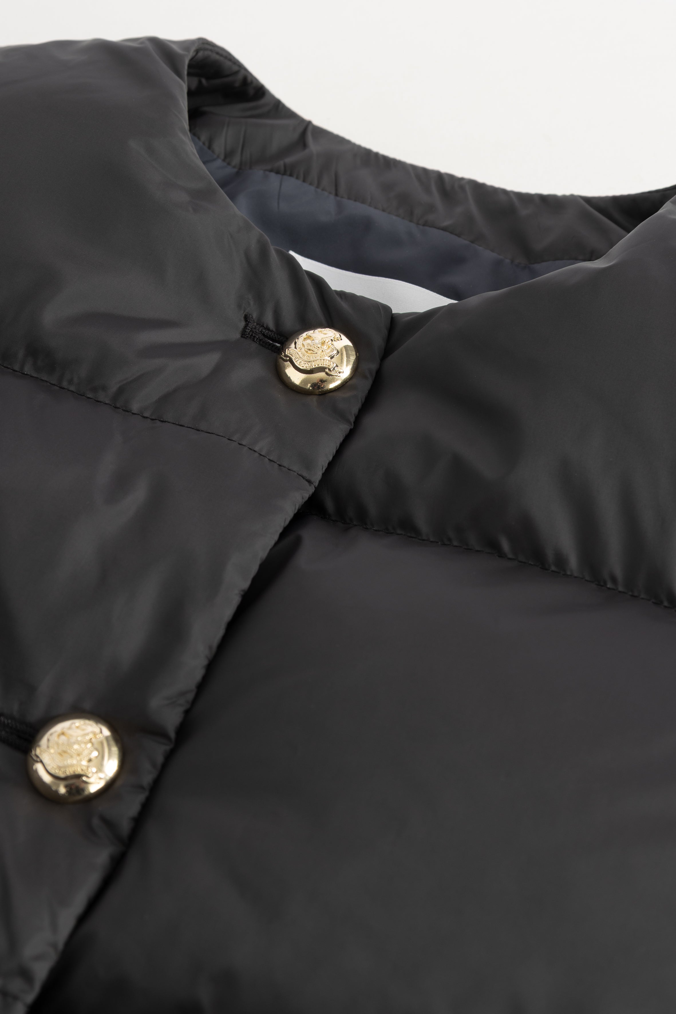 Close-up of a black LEMPELIUS puffer jacket with gold buttons on a white background