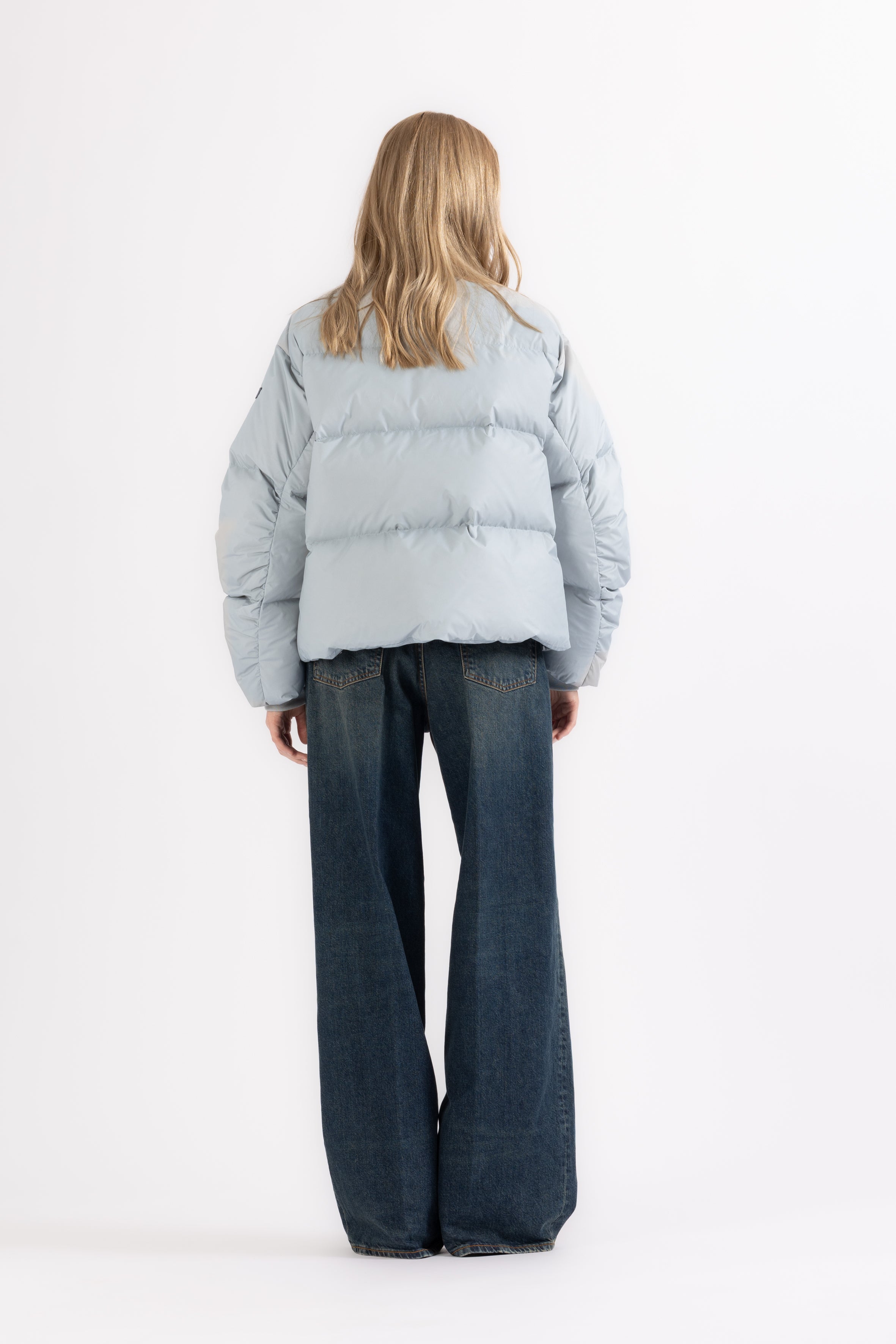 Person wearing a light blue puffer jacket and dark jeans on a white background